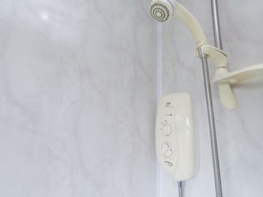 A close up of a wall mounted electric shower system with a handheld showerhead and hose in a shower cubicle at Seafield in Rhydwyn near Cemaes Bay
