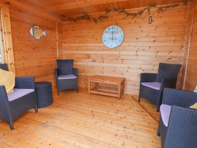 A wooden room with four black wicker chairs with cushions a small wooden table and a clock on the wall at Seafield in Rhydwyn near Cemaes Bay
