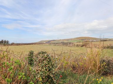A field with bushes in the foreground and hills in the background at Seafield in Rhydwyn near Cemaes Bay