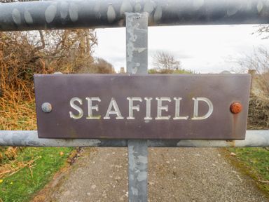 A metal gate with a sign reading Seafield on a rural path at Seafield in Rhydwyn near Cemaes Bay