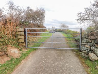 A metal gate across a paved country road with bushes and trees on either side at Seafield in Rhydwyn near Cemaes Bay