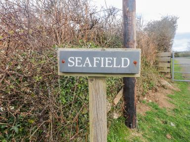 A wooden signpost with the word Seafield next to a dirt path and hedges at Seafield in Rhydwyn near Cemaes Bay