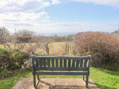A black garden bench overlooking a grassy field and hedges with a view of the sea at Seafield in Rhydwyn near Cemaes Bay