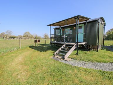 A shepherds hut with a covered porch and stairs in a grassy fenced field at Gilberry Shepherds Hut in Wall under Heywood near Church Stretton