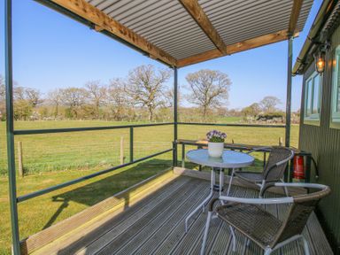 An outdoor seating area with two chairs a small table and a potted plant overlooking a grassy field at Gilberry Shepherds Hut in Wall under Heywood near Church Stretton