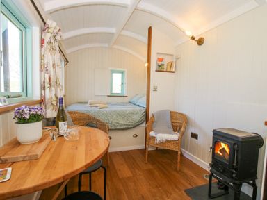 A small room with a bed towels wicker chairs a wood stove and a wooden table with wine at Gilberry Shepherds Hut Wall under Heywood near Church Stretton