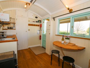 A small kitchen area with a sink, toaster, microwave and shelves next to a wooden fold-down table with two stools at Gilberry Shepherds Hut Wall under Heywood near Church Stretton