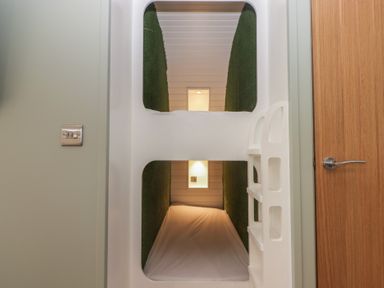 A room with white bunk beds and green wall panels with a wooden door on the right