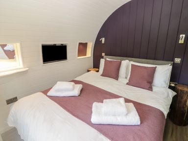 A bedroom with a double bed white and purple bedding towels on bed and a wall-mounted TV at The Hazel Pod in Cowbridge