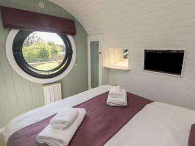 A bedroom with a round window a bed with folded towels a wall-mounted TV and a small mirror at The Hazel Pod in Cowbridge
