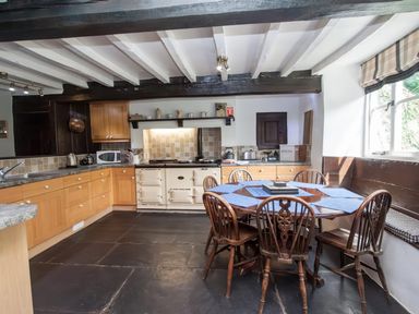 A kitchen with wooden cabinets round dining table wooden chairs and window seat at The Cragg in Hawkshead