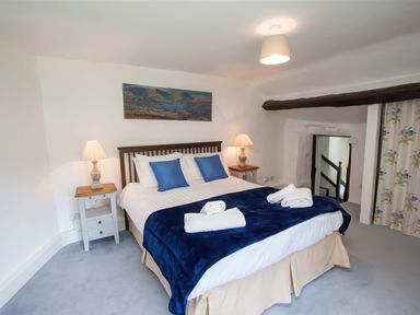 A bedroom with a double bed with blue pillows and blanket two bedside tables with lamps and a painting on the wall at The Cragg in Hawkshead
