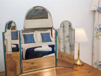 A bedroom reflected in a three panel mirror with a bedside lamp and floral curtains at The Cragg in Hawkshead