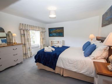 A bedroom with a double bed with blue pillows and blanket a dresser with a mirror and floral curtains at The Cragg in Hawkshead