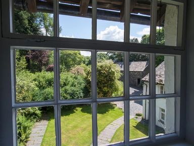 A window view showing a garden with grass and bushes stone pathway and buildings at The Cragg in Hawkshead