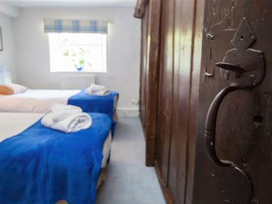 A bedroom with two single beds covered with blue blankets and folded towels near a window with plaid blinds at The Cragg in Hawkshead