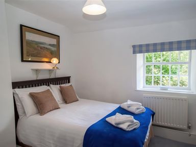 A bedroom with a bed with pillows and folded towels in front of a window with a blue check curtain at The Cragg in Hawkshead