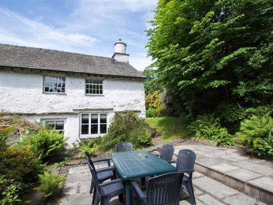 An outdoor patio with a table and chairs next to a white house surrounded by greenery at The Cragg in Hawkshead