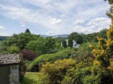 A garden with various trees and bushes and a white house in the background at The Cragg in Hawkshead
