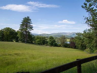 A grassy field with trees and hills in the distance under a blue sky at The Cragg in Hawkshead