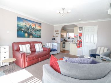 A living room with a red leather sofa, three armchairs, a small round table, and an open kitchen at 98 Waterside Park in Corton