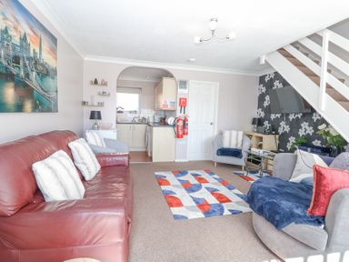 A living room with a red leather sofa, two armchairs, a patterned rug, a wall-mounted TV, and a view into a kitchen at 98 Waterside Park in Corton