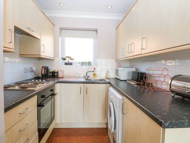 A kitchen with light wood cabinets black countertops a stove oven washing machine microwave and window at 98 Waterside Park in Corton