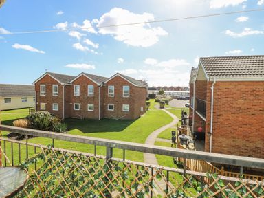 A view of brick residential buildings with a paved pathway and green lawn at 98 Waterside Park in Corton