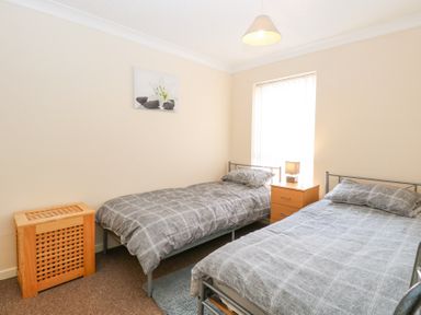 A bedroom with two single beds a wooden nightstand with a lamp a wooden laundry basket and a flower picture on the wall at 98 Waterside Park in Corton