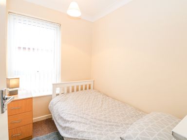 A small bedroom with a single bed next to a wooden drawer and window with vertical blinds at 98 Waterside Park Corton