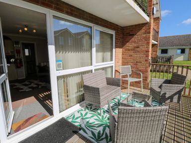 A balcony with wicker chairs and a small table and a chair on a patterned rug at 98 Waterside Park Corton