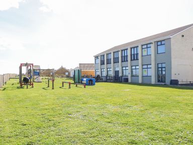 A playground with climbing and obstacle equipment on grass next to a two story building at 98 Waterside Park in Corton