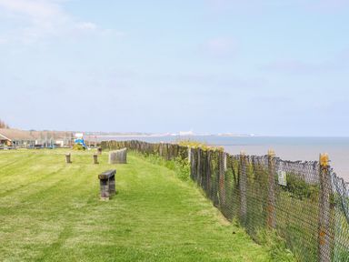 A grassy area with benches and a fence overlooking water and houses in the distance at 98 Waterside Park in Corton
