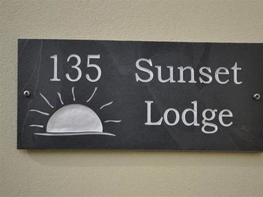A black rectangular sign with the number 135 a sunrise illustration and the words Sunset Lodge