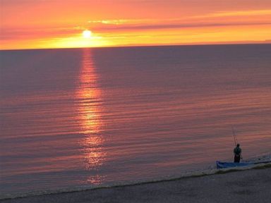 A person fishing on a beach at sunset over calm sea at Sunset Lodge in Fortuneswell