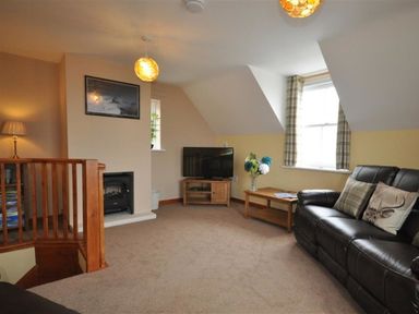 A living room with a leather sofa a wooden coffee table a television and a staircase at Sunset Lodge in Fortuneswell