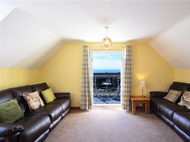 A living room with two leather sofas cushions side table lamp and balcony with table and chairs overlooking the sea at Sunset Lodge in Fortuneswell