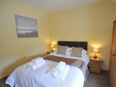 A bedroom with a double bed two bedside tables with lamps and a wooden wardrobe at Sunset Lodge in Fortuneswell
