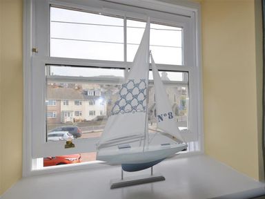 A model sailboat on a windowsill with buildings and cars outside the window at Sunset Lodge in Fortuneswell