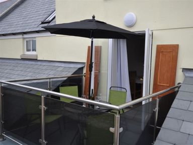 A balcony with a black umbrella green chairs and a table with glassware at Sunset Lodge in Fortuneswell