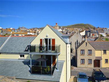 A building with balconies and open doors overlooking a street with parked cars and houses in the background at Sunset Lodge in Fortuneswell