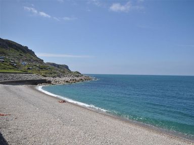 A pebble beach with a rocky shoreline hill and blue sea at Sunset Lodge in Fortuneswell