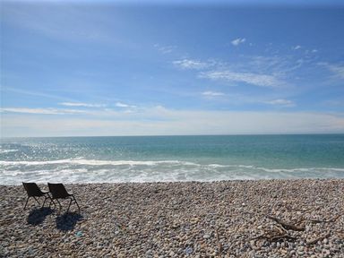Two chairs on a pebble beach facing the ocean under a partly cloudy sky at Sunset Lodge in Fortuneswell