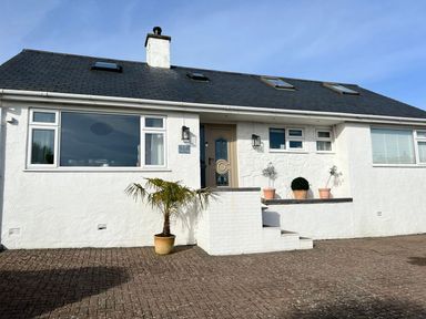 The exterior of a white house with potted plants near the entrance at Trem Ynys 3 bed in Abersoch