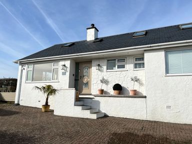 The exterior front of a white house with steps leading to a beige door and potted plants on the porch at Trem Ynys 3 bed in Abersoch