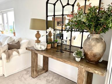 A wooden console table with a large mirror lamp plants and decorative items beside a white sofa in a living room at Trem Ynys 3 bed in Abersoch