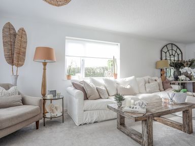 A living room with a white sofa beige armchair wooden coffee table and decorative plants at Trem Ynys (3 bed) in Abersoch
