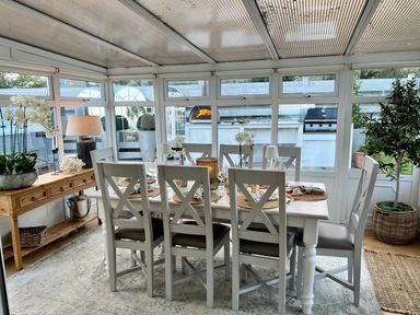 A dining room with a table set for a meal surrounded by chairs and a wooden console table with plants at Trem Ynys 3 bed in Abersoch
