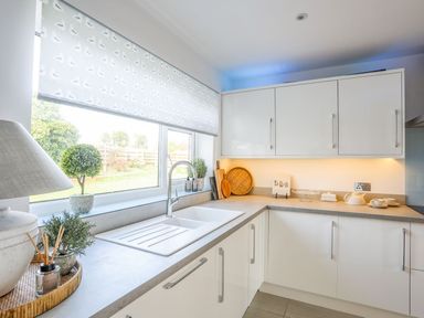 A kitchen with white cabinets a sink and a window with a patterned blind at Trem Ynys (3 bed) in Abersoch