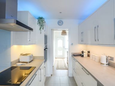 A galley kitchen with white cabinets and appliances at Trem Ynys (3 bed) in Abersoch